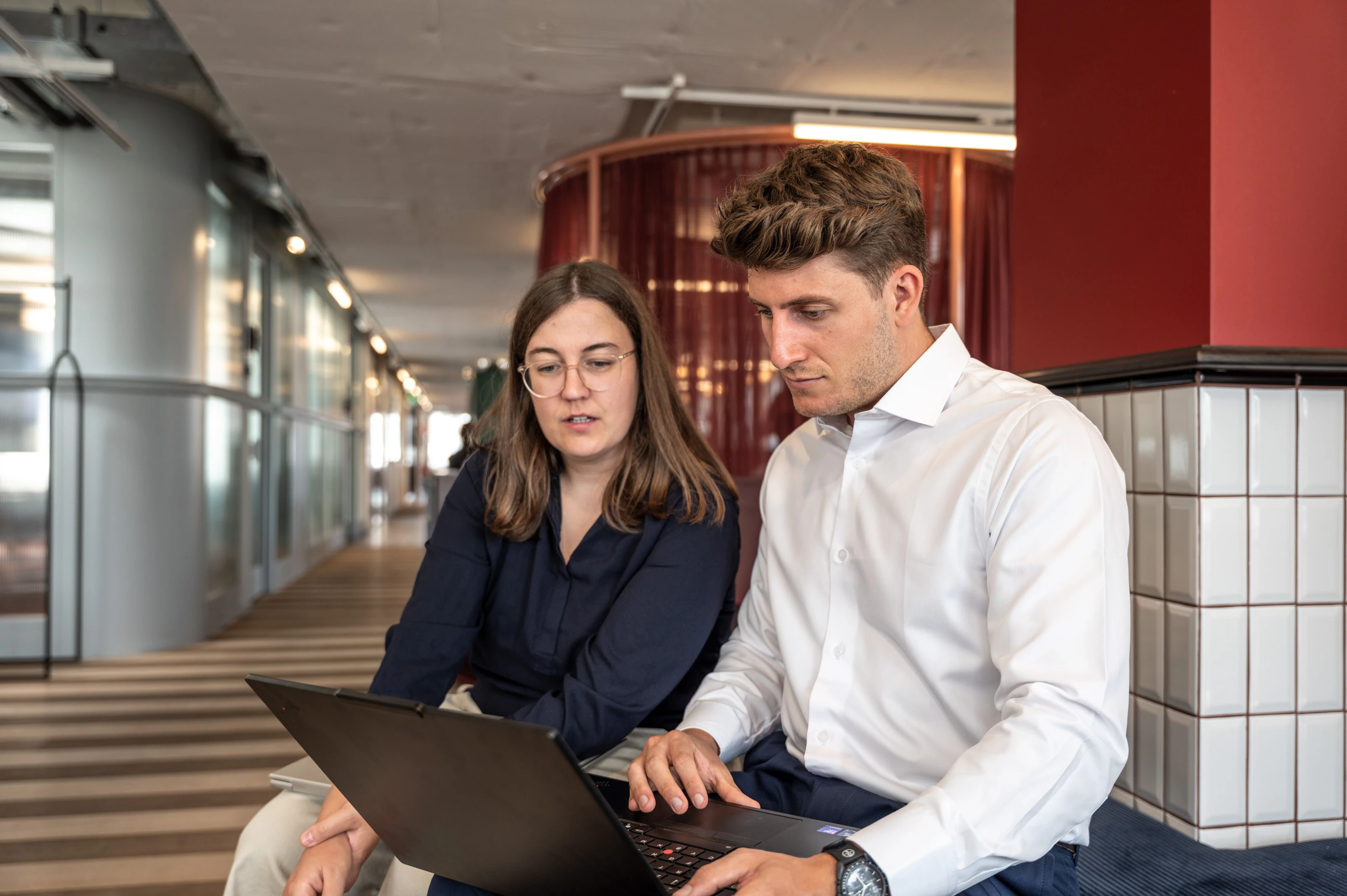 Zwei Teammitglieder arbeiten im Flur gemeinsam am Laptop