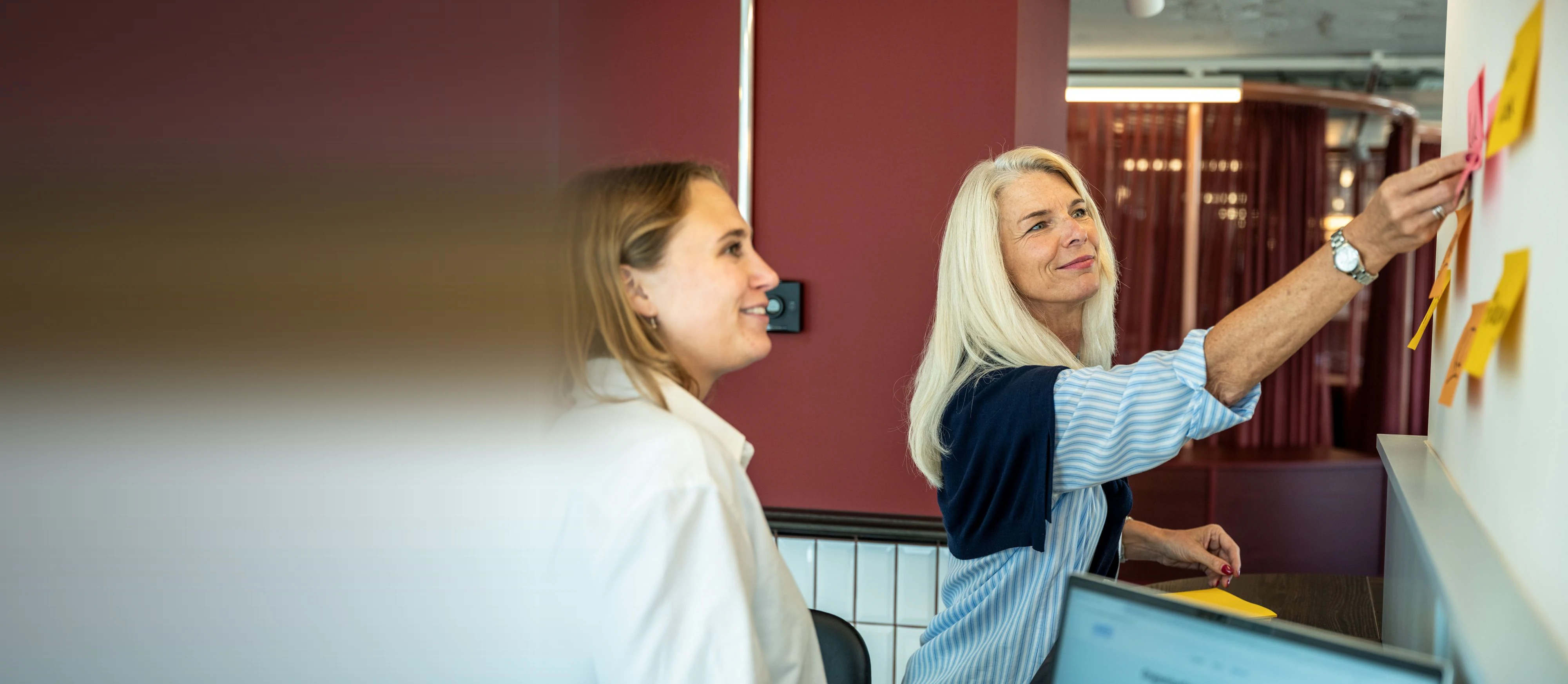 Kerstin Rufer, Managing Partner, ordnet mit einer Kollegin Notizzettel an einer Wand
