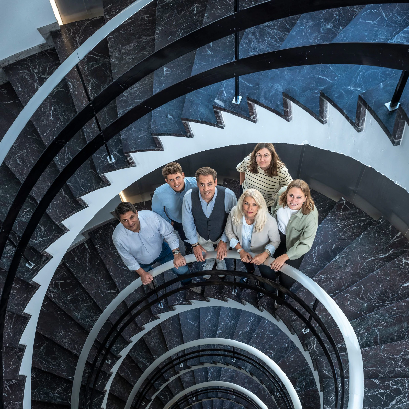 Das Team von Pfyffer Partner in einem Treppenhaus mit Wendeltreppe, von oben fotografiert